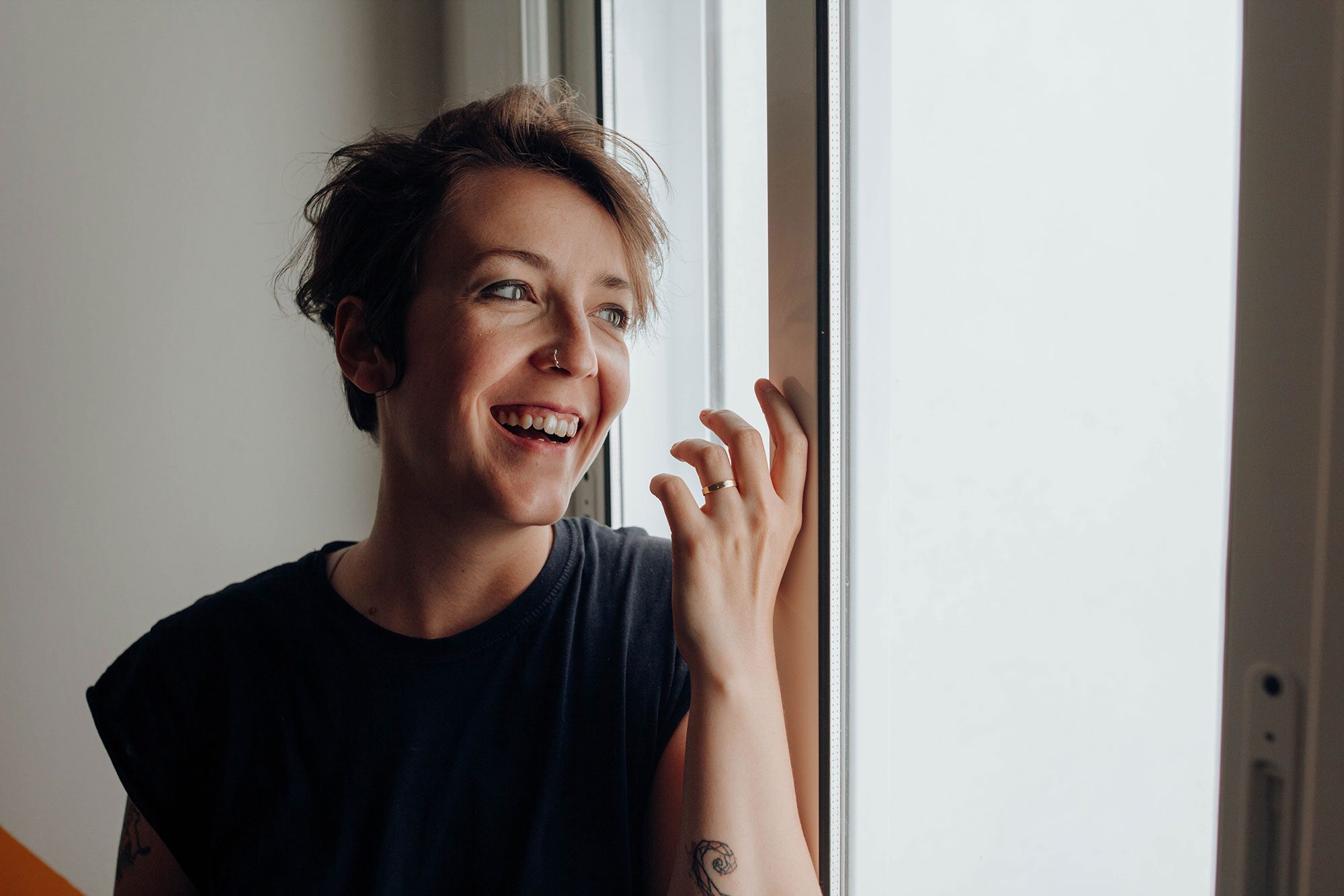 A disabled person with feminine features and short hair looks out the window and smiles.