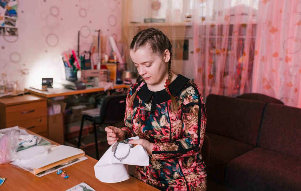 A disabled woman wearing a floral dress is doing a craft in her home.