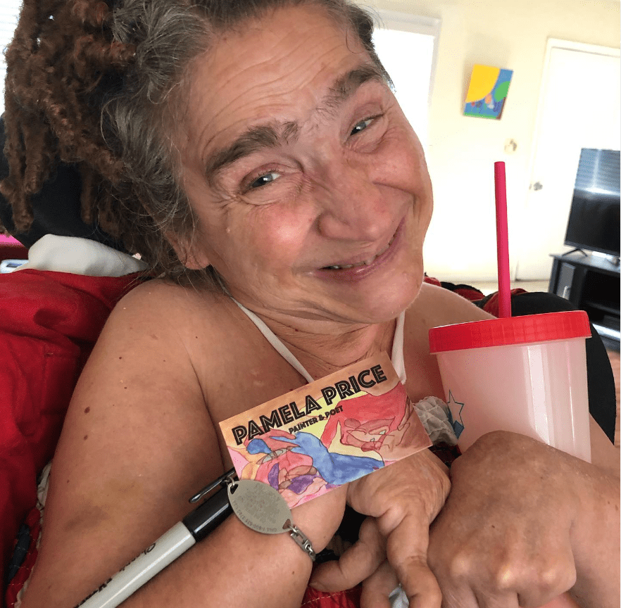 Pam smiles brightly at the camera while holding her Painter and Poet business card
