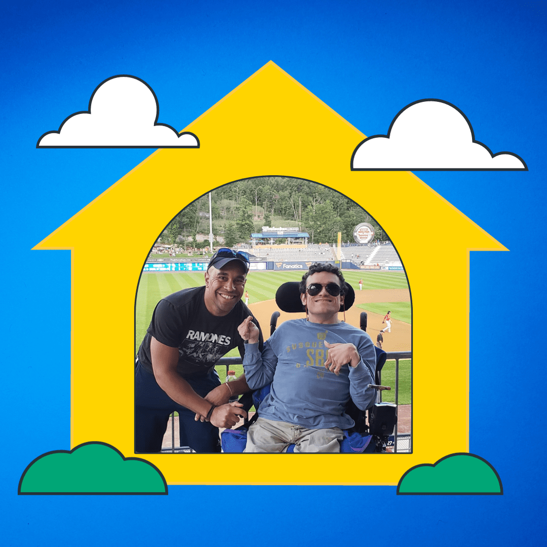 Blue background with a yellow shape of a house with white clouds and green bushes. In the house is a picture of two men. One is standing and the other is sitting in a power wheelchair. Both are smiling at the camera.